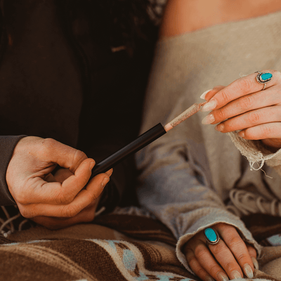 Close-up of two hands exchanging a small tube, showcasing a stylish and cozy outdoor setting.