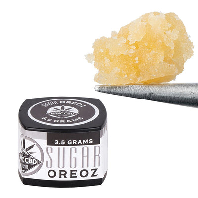 WNC CBD THCA Sugar in a black container with a cannabis sugar sample on a tool, perfect for enhancing smoking experiences.
