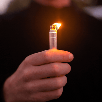 A person holding a refillable lighter with a flame, perfect for outdoor adventures and convenience.
