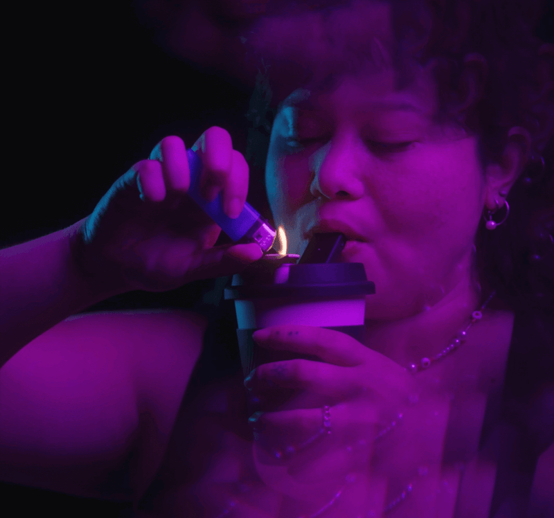 Person using Puffco Cupsy Coffee Cup Water Pipe under vibrant lighting, demonstrating its discreet design and functionality.